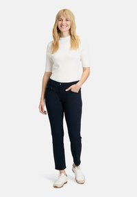 Tummansiniset kapeat housut, joissa on huomaamattomat etutaskut, yhdistettynä tiukkaan valkoiseen toppiin. Asennetta täydentävät valkoiset lenkkarit.