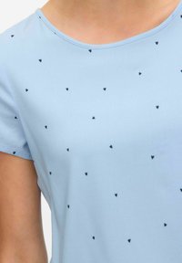 Lichtblauw kort mouwtopje van zachte stof, met een ronde hals en verspreide kleine zwarte hartjespatronen.
