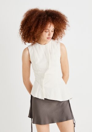 White sleeveless top with a pleated texture and peplum hem. Paired with a gray mini skirt featuring adjustable ties on either side.