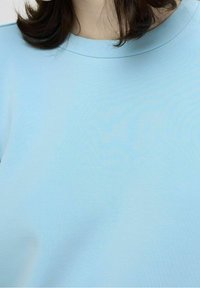 Camiseta de manga corta azul claro hecha de una tela suave. Textura lisa con un escote redondo y un corte holgado. Sin patrones ni acentos visibles.