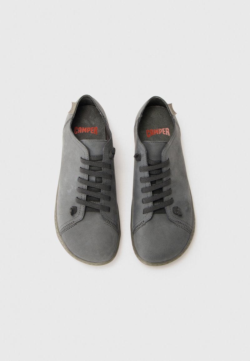 Paio di scarpe casual in pelle grigia con lacci neri, suole in gomma e logo rosso "Camper" sulle suole interne, viste dall'alto.