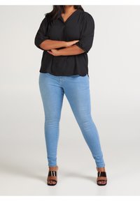 Černá blůza s krátkým rukávem a výstřihem do V; v kombinaci se světle modrými skinny džíny; model má na sobě hnědé sandály na podpatku. Jednoduchý a uvolněný design.