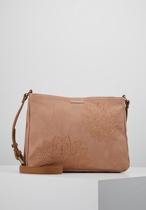 Sac bandoulière marron clair avec motifs floraux brodés et bandoulière réglable, exposé sur un socle blanc sur fond neutre.