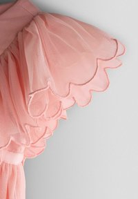 Hellrosa Tüllkleid mit Rüschenärmeln und gewellten Kanten. Das Material ist durchsichtig und weich, mit einem gerafften Taillenbund für einen fließenden Look.