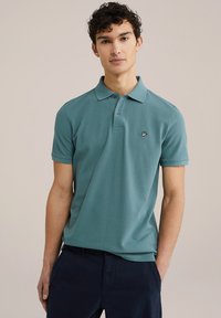 Camisa polo de color verde azulado, hecha de algodón, con mangas cortas, una tapeta de tres botones y logo bordado en el lado izquierdo del pecho.
