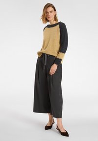 Żółto-granatowy sweter o strukturalnym wykończeniu, połączony z szerokimi, ciemnoszarymi spodniami i brązowymi butami z weluru. Prosty, casualowy design.