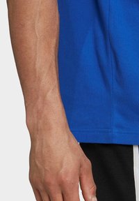 Modré bavlněné tričko s hladkou strukturou, krátkými rukávy a rovný lem, v kombinaci s černými šortkami s bílými pruhy.