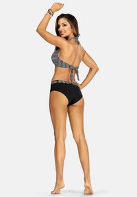 Czarny i biały zestaw bikini z wzorzystą górą i jednolitymi czarnymi majtkami. Góra ma wiązanie z tyłu, płaskie szwy i wygodne dopasowanie.