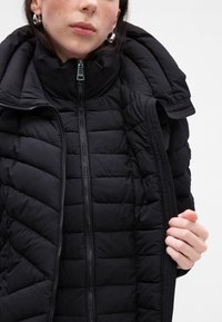 Giacca a vento nera con colletto alto, motivo trapuntato e chiusura con zip. Tessuto liscio e vestibilità comoda con cappuccio.