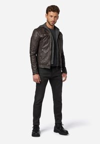 Brun läderbikerjacka med kviltade axeldetaljer, grå huvtröja under, kombinerat med svarta jeans och svarta snörstövlar.