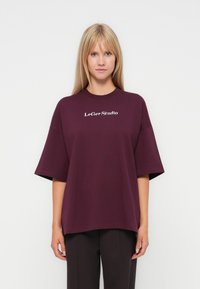 Burgundy oversized t-shirt made of cotton, featuring a round neckline and short sleeves. Text "LeGer Studio" printed in white on the front.