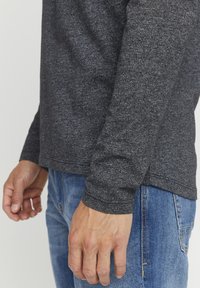 Langärmliges Shirt aus dunkelgrauem Strickstoff mit abgerundetem Saum und gerippten Bündchen, kombiniert mit hellblauen Jeans.