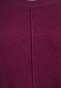 Gros plan sur un pull violet foncé avec un col côtelé et une couture centrale descendant dans le dos. Texture douce et tricotée visible.