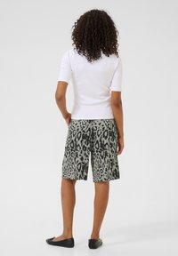 Top blanco ajustado de manga corta, combinado con pantalones cortos verdes con un estampado de leopardo negro. El modelo lleva zapatos planos negros. Diseño simple, estilo informal.