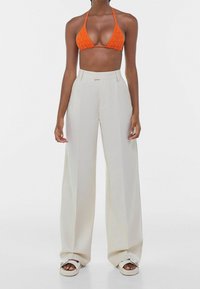 Crochet oranžový bikiny top a krémové kalhoty s vysokým pasem a širokými nohavicemi. Hladká tkanina s řaseným vzorem a volným střihem. Platformové sandály.