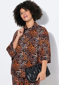 Leopardpræget skjorte i orange, sort og hvid; knap-down design med korte ærmer. Sammen med en sort quiltet clutch-taske.