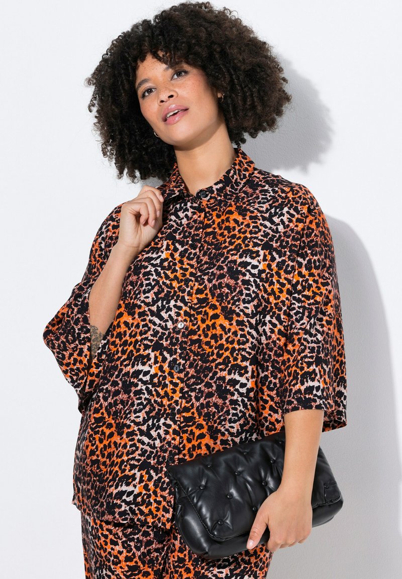 Leopardpræget skjorte i orange, sort og hvid; knap-down design med korte ærmer. Sammen med en sort quiltet clutch-taske.