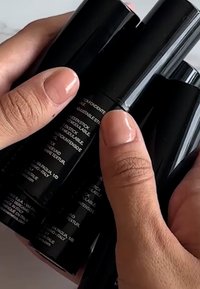 Fire svarte makeup-pinner holdt i hendene, med glatte matte overflater og pregete etiketter med produktinformasjon på flere språk.