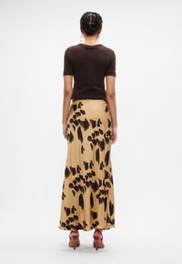 Vrouw die met haar rug naar de camera staat, gekleed in een bruin topje met korte mouwen, een beige rok met zwarte abstracte vlekken, rode hoge hakken en ringoorbellen.