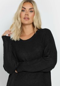 Maglione nero a coste, con maniche lunghe e una scollatura ampia, dal taglio morbido. Il tessuto testurizzato aggiunge profondità, con spalle ribassate per maggiore comfort.