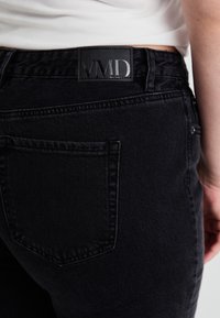 Black denim jeans with a smooth texture and minimalistic design. Features a VMD logo patch on the back waistband and a single pocket detail.