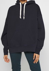 Mörkblå hoodie av mjukt tyg, med känguruficka, huva med dragsko och ribbade muddar. Enkel, avslappnad design.