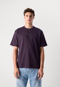 T-shirt en coton violet à manches courtes et col rond. Présente un logo "BOSS" subtil sur la poitrine. Porté avec un jean en denim bleu clair.