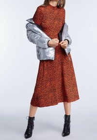 Punainen leopardikuvioinen midimekko, joka on yhdistetty kiiltävään hopeanväriseen untuvatakkiin; mustat nyörilliset nilkkurit täydentävät asun.