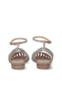 Sandalias planas beige con tiras metálicas plateadas, diseño entrelazado y hebilla en el tobillo. Plantilla suave y lisa con una ligera textura. Estilo de punta abierta.