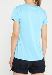 Světle modré tričko s krátkými rukávy a kulatým výstřihem, vyrobené z měkké látky. Kombinováno s tmavými kraťasy s ohrnutými lemy.