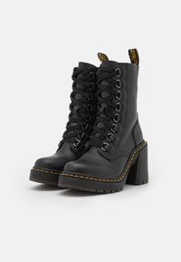 Stivali in pelle nera con tacco, caratterizzati da un design con lacci, cuciture gialle ben visibili e una suola gommata. Presentano hardware in argento e tacchi a blocco alti.