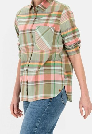 Frau trägt ein pastellfarbenes kariertes Hemd mit hochgekrempelten Ärmeln und blaue Jeans, dargestellt vom mittleren Oberkörper bis zu den Hüften.