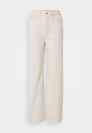 Lyse beige vide jeans laget av bomull. Har høy midje, knappelukking foran og to horisontale sømdetaljer på beina.