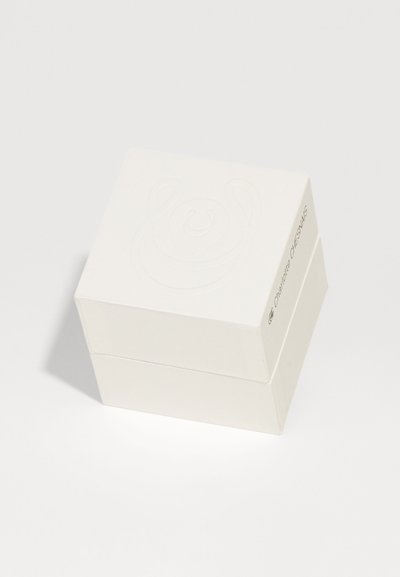 Biely obdĺžnikový box s textúrovaným vekom a s reliéfnym dizajnom. Na boku je zobrazené branding v jednoduchom písme. Hladký matný povrch.