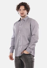 Camicia a maniche lunghe grigia chiara con motivi geometrici scuri. Presenta un colletto classico, maniche lunghe e una vestibilità rilassata.