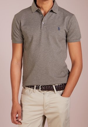 Szary bawełniany polo z kołnierzykiem i trzema guzikami, z małym niebieskim logo. Nosi się z kremowymi spodniami i plecionym brązowym paskiem.