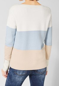 Stickad tröja med breda randiga mönster i vitt, ljusblått och beige. Har en rundad hals och långa ärmar. Mjuk textur.