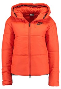 Orange fodrad jacka med huva, utrustad med en svart dragkedja och Nike-logotyp. Insidan har ett kontrasterande mönster längs huvens kant.