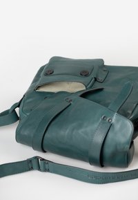 Teal leren tas met een gestructureerde vorm, een klep bovenkant, zakdetails en een verstelbare schouderband. Interieur met een gestreepte voering.