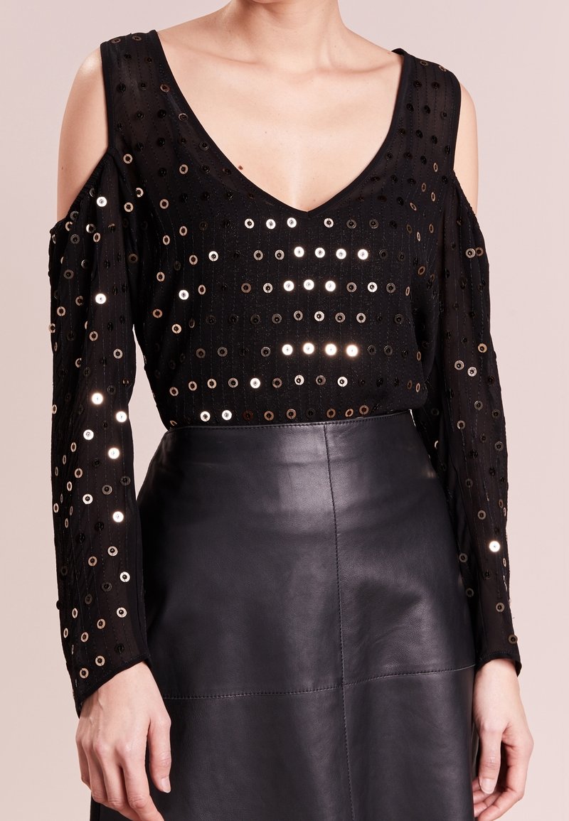 Top nero a maniche lunghe con scollatura a V, con spalle tagliate e decorazioni metalliche. Abbinato a una gonna in pelle nera elegante.