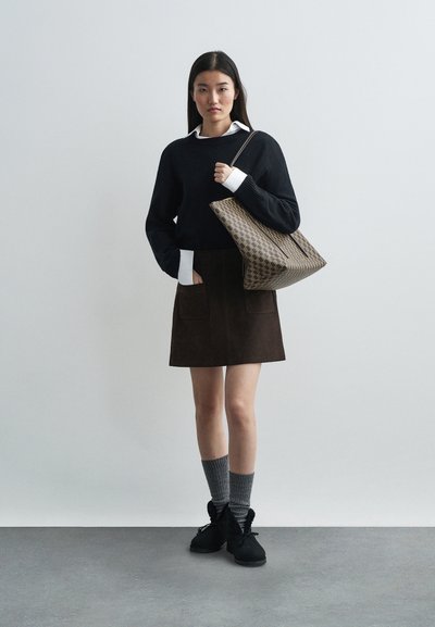 Black knit sweater with white cuffs, brown suede skirt with pockets, gray knitted socks, black ankle boots, and a patterned tote bag.