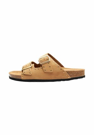 Tan suede slide sandal med to justerbare remme, pyntet med sølvnitter. Sålen er lavet af kork med en sort gummisål.