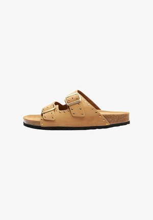 Tan suede slide sandal med to justerbare remme, pyntet med sølvnitter. Sålen er lavet af kork med en sort gummisål.