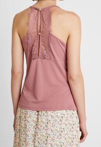 Dammig rosa ärmlös topp med spetsdetaljer på baksidan, med en nyckelhålsöppning säkrad av två knappar. Mjuk textur; enkel design.