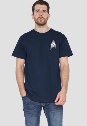 Navy blue cotton t-shirt featuring a metallic silver design resembling a starship insignia on the left chest area. Short sleeves, classic fit.
