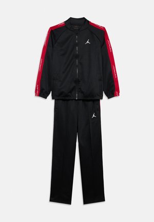 Schwarzer Trainingsanzug mit Reißverschluss, roten Streifen an den Ärmeln und weißen Jumpman-Logos auf der Brust und am linken Hosenbein, flach auf weißem Hintergrund ausgelegt.