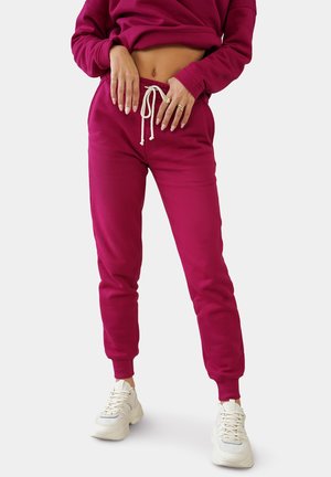 Fuchsia sweatpants med snor i taljen, ribbede manchetter og blødt materiale, parret med hvide sneakers.