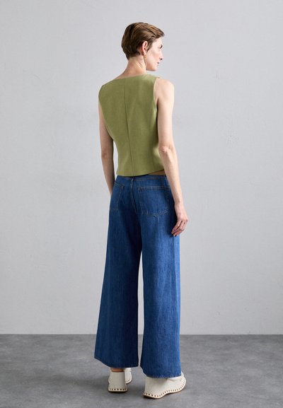 Top sin mangas de color verde oliva con un diseño ajustado, combinado con jeans de mezclilla azules sueltos. El conjunto se completa con zuecos de color crema.