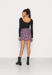 Camisola preta de mangas longas com costas em forma de cavalo, combinada com uma saia mini de padrão floral com flores rosas e roxas, e botas de salto pretas.
