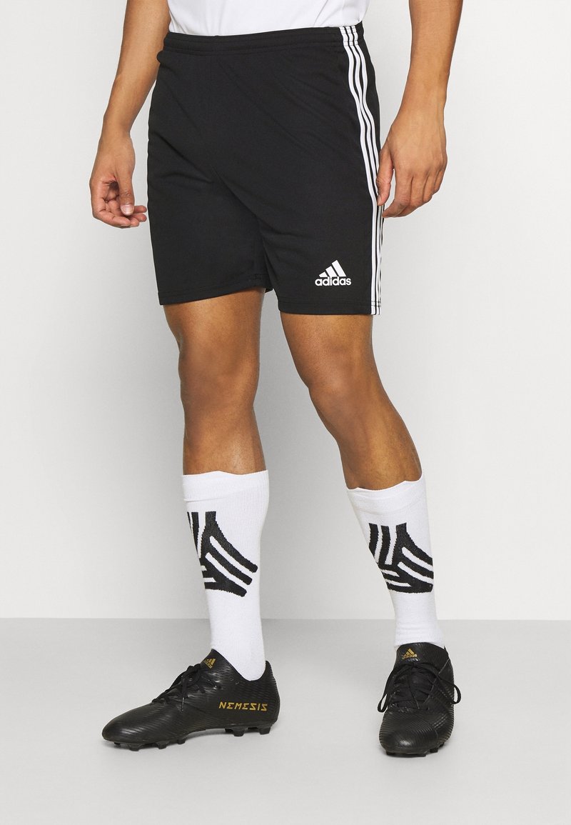 Shorts de sport noirs avec des rayures blanches sur les côtés, associés à des chaussettes blanches montantes avec un design abstrait noir et des crampons noirs.